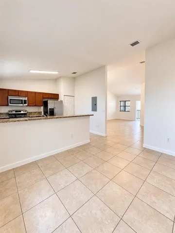 Kitchen featuring wood cabinetry, stone-finish countertops, and stainless steel appliances, accented by large-format tile flooring and vaulted ceilings