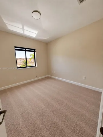 Neutral-toned wall interior featuring plush wall-to-wall carpeting, a single-pane window with a black frame, and a flush-mount circular ceiling light