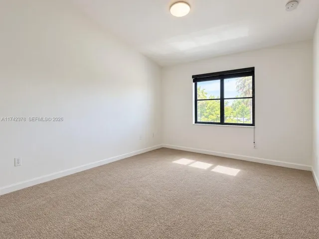Neutral interior featuring wall-to-wall carpeting, vaulted ceiling, and a large window with a black frame