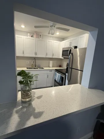 Kitchen featuring white cabinetry, stainless steel appliances, a white ceiling fan, recessed lighting, and a speckled light-toned countertop