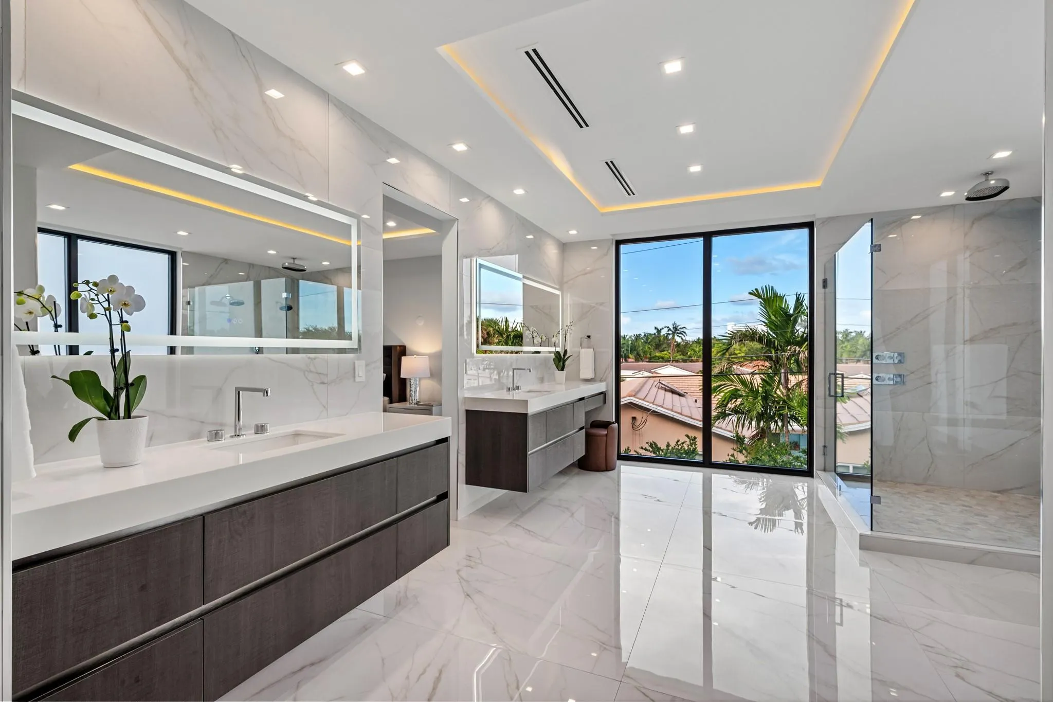 An expansive, light-filled bath retreat featuring dual floating vanities, a sleek glass-enclosed shower, and refined contemporary finishes throughout. Seamlessly connected to a private terrace, this spa-inspired space offers tranquil views and effortless indoor-outdoor luxury.