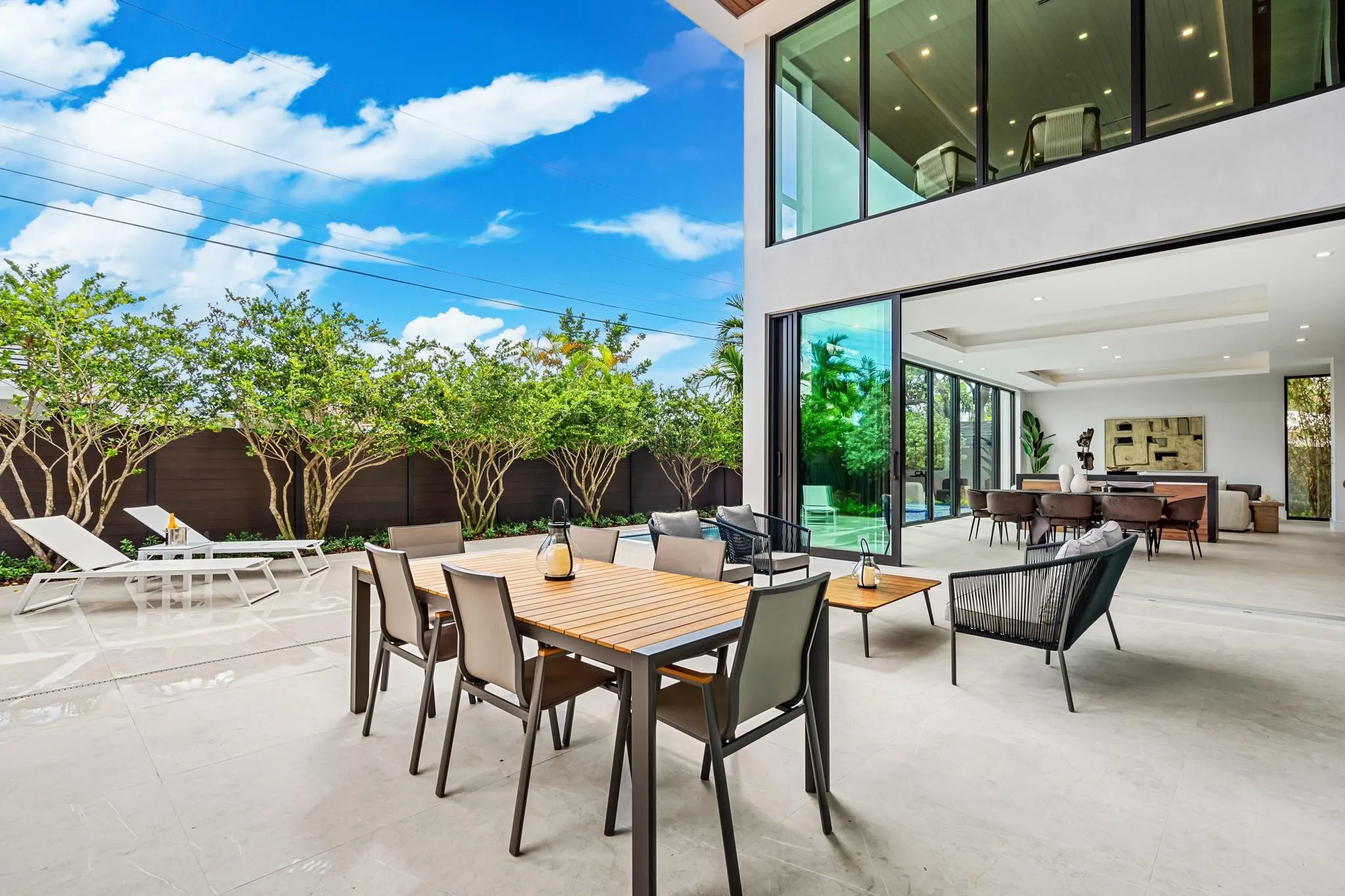 An expansive covered outdoor terrace designed for seamless entertaining, featuring a spacious dining area and comfortable lounge seating overlooking lush tropical landscaping. Modern and open, this inviting space extends the home’s living areas into a private resort-style setting.