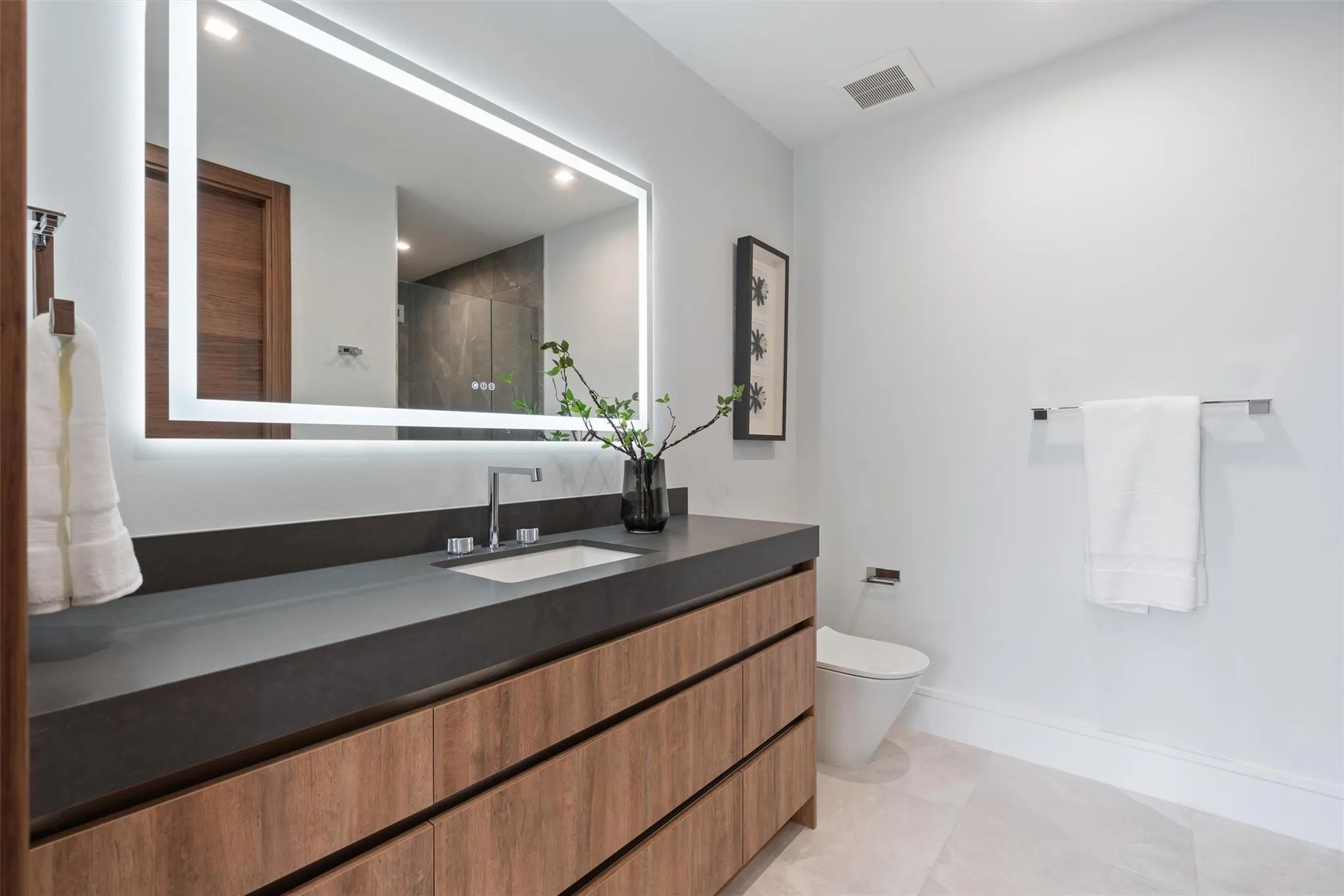 A sleek, modern bath showcasing a floating wood vanity, expansive mirror, and clean-lined contemporary finishes. Bright and minimalist, this refined space offers spa-like simplicity with warm, natural accents.