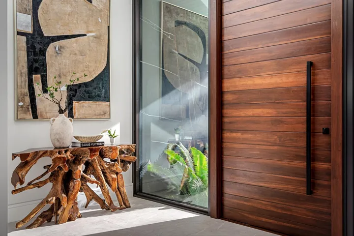 A sophisticated entry detail featuring a striking wood pivot door, sleek glass panels, and curated contemporary art that creates an immediate design statement. Warm natural textures and clean modern lines set a tone of refined luxury from the moment you arrive.