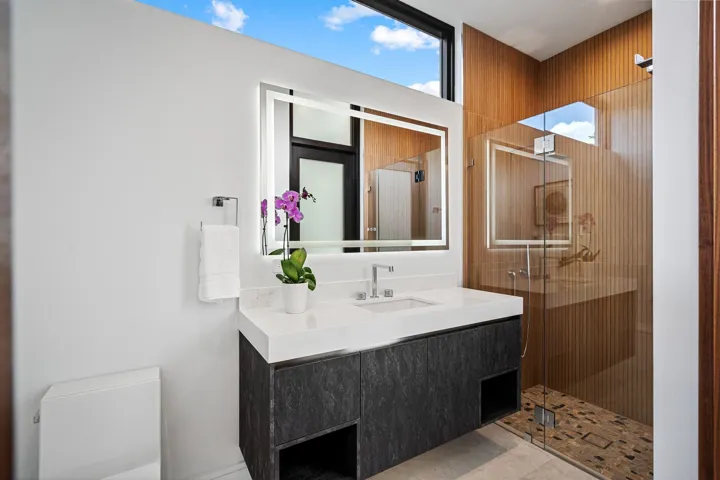 A sleek contemporary bath featuring a floating vanity with bold stone countertop, designer fixtures, and warm accent tones. Clean lines and modern finishes create a refined, spa-inspired retreat for guests.