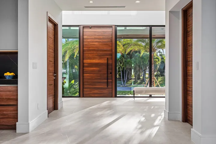 A grand modern entry framed by warm wood accents, floor-to-ceiling glass, and abundant natural light. Clean architectural lines and a dramatic pivot door create a striking first impression of contemporary sophistication.