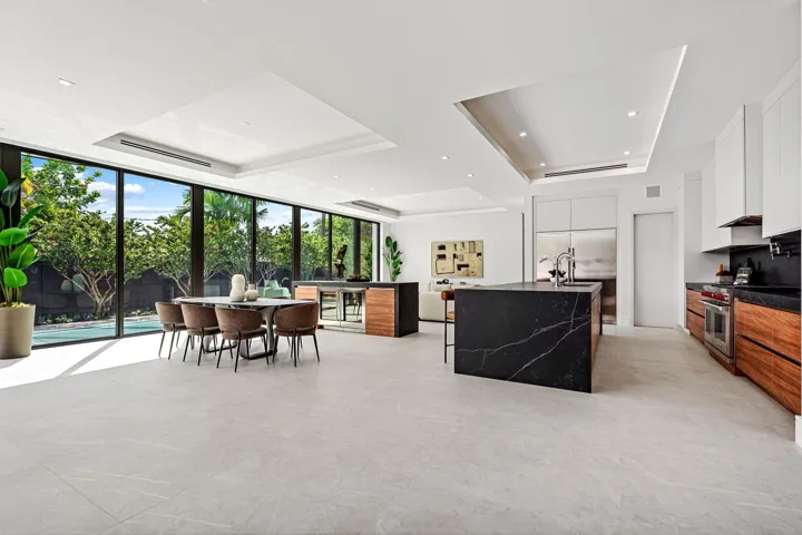 An expansive open-concept living and dining area defined by soaring ceilings, clean modern lines, and walls of glass that invite the outdoors in. Seamlessly connected to the covered terrace and lush surroundings, this light-filled space embodies effortless contemporary living.