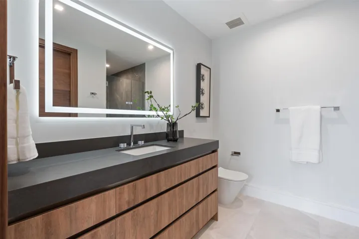 A sleek, modern bath showcasing a floating wood vanity, expansive mirror, and clean-lined contemporary finishes. Bright and minimalist, this refined space offers spa-like simplicity with warm, natural accents.