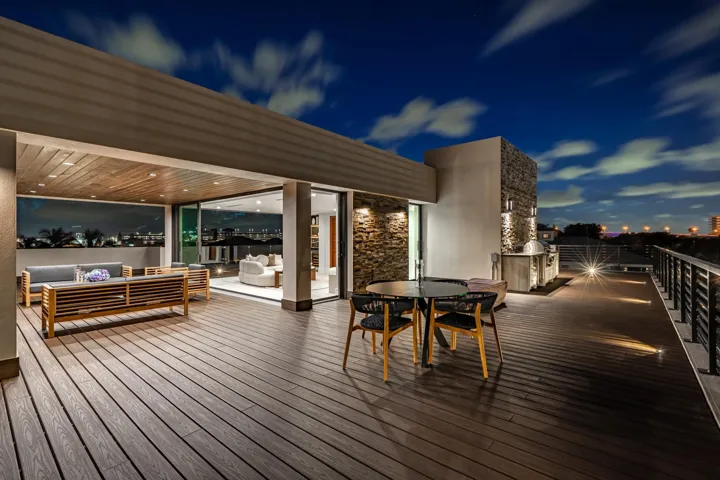 A dramatic evening terrace showcasing expansive decking, warm ambient lighting, and multiple lounge areas designed for effortless entertaining. Elevated and atmospheric, this stunning outdoor space captures the essence of modern luxury under the night sky.