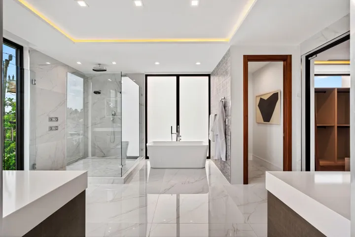 A spa-caliber primary bath featuring a freestanding soaking tub, expansive walk-in shower, and sleek floating vanities framed by warm wood accents. Light-filled and impeccably finished, this serene retreat embodies modern luxury and refined tranquility.