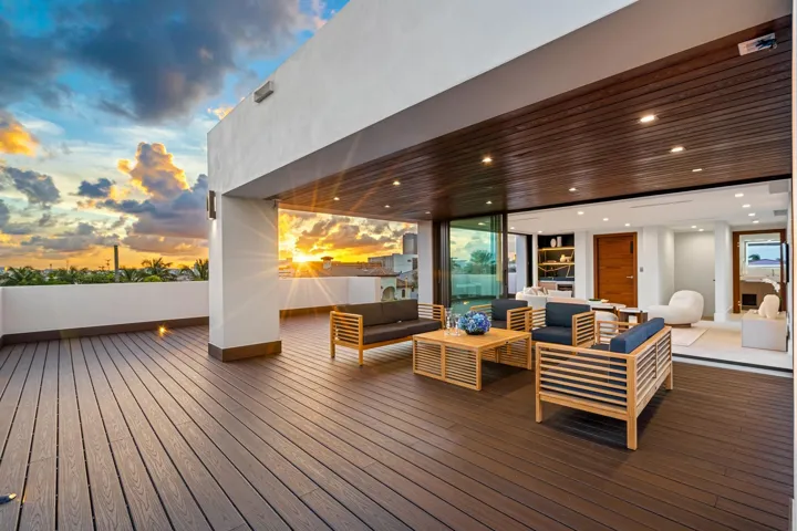 An expansive covered terrace featuring warm wood ceilings, elegant lounge seating, and seamless flow to the open-air deck beyond. Framed by breathtaking sunset skies, this sophisticated outdoor retreat is designed for elevated entertaining and relaxed coastal evenings.