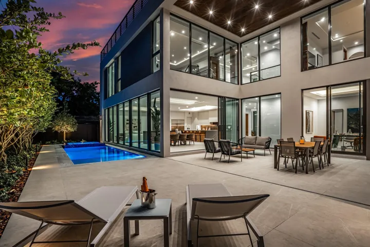 A breathtaking glass-wrapped courtyard illuminated at twilight, where soaring ceilings and expansive windows create a seamless indoor-outdoor experience. Refined lounge and dining spaces are beautifully positioned for sophisticated entertaining in a dramatic modern setting.