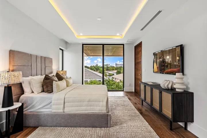 A refined modern bedroom retreat featuring custom ceiling detailing, warm wood accents, and expansive glass doors opening to lush outdoor views. Sophisticated and serene, this private sanctuary blends contemporary design with effortless indoor-outdoor living.