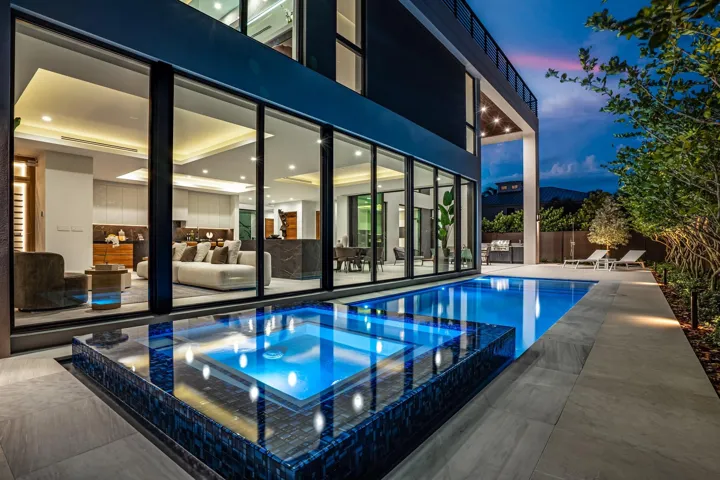 A dramatic evening poolscape framed by floor-to-ceiling glass walls that dissolve the boundary between indoors and out. Sleek, modern, and illuminated to perfection, this stunning setting captures the essence of sophisticated living after dark.