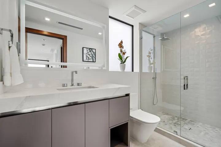 A sleek contemporary bath featuring a streamlined floating vanity, expansive mirror, and crisp white finishes accented by warm wood tones. Clean, bright, and elegantly appointed, this spa-inspired space offers refined comfort with modern sophistication.