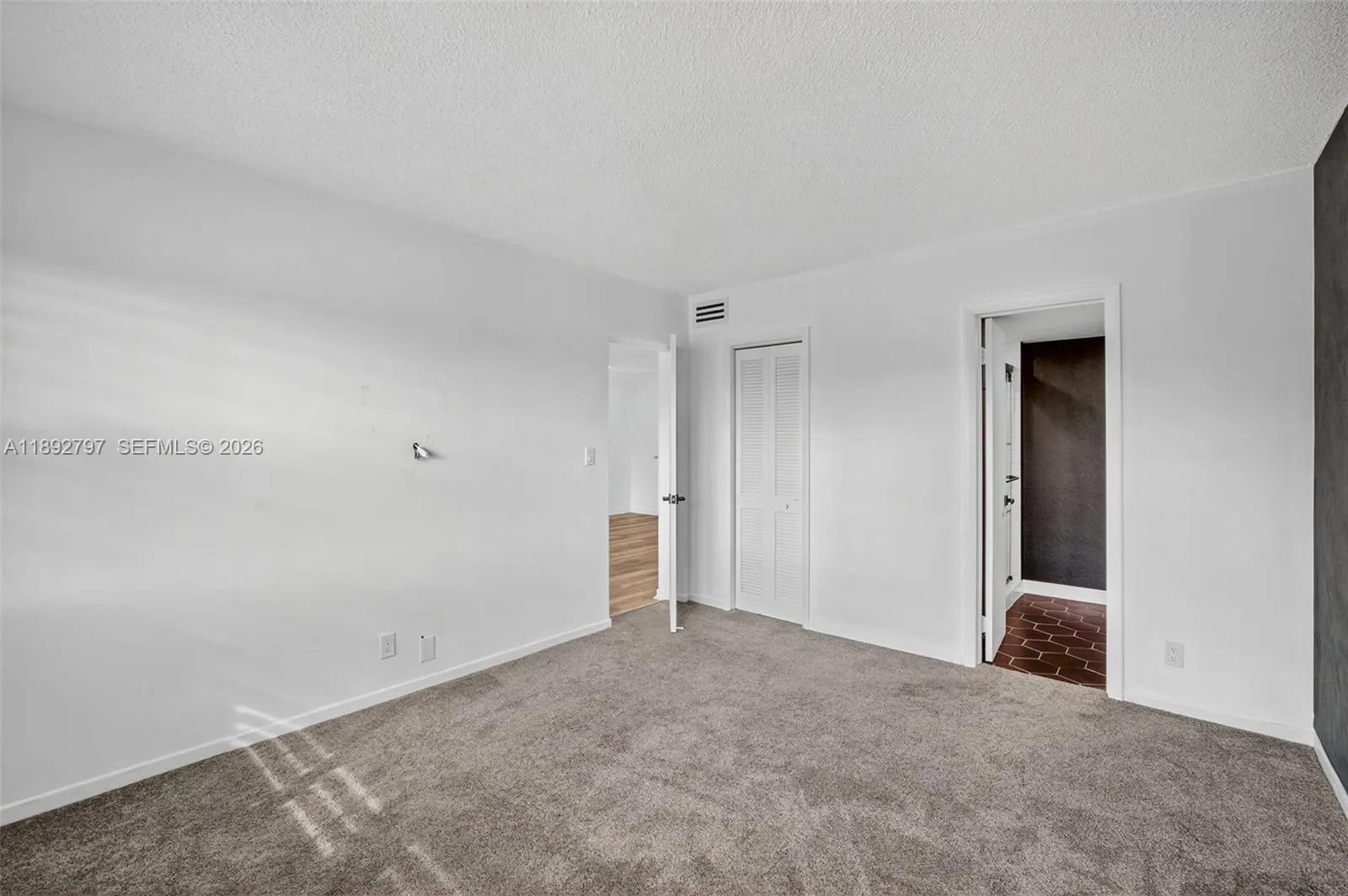 Primary Bedroom w/ Impact Windows, louvered shutters, wallpapered feature wall and newer carpet in amazing condition. Flat ceilings