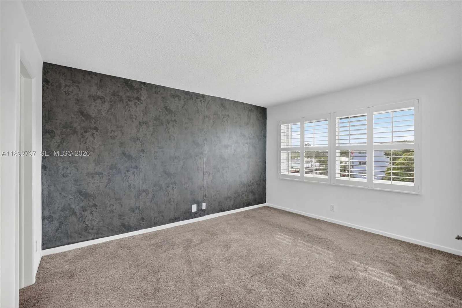 Primary Bedroom w/ Impact Windows, louvered shutters, wallpapered feature wall and newer carpet in amazing condition leading to ensuite bathroom and walk in closet