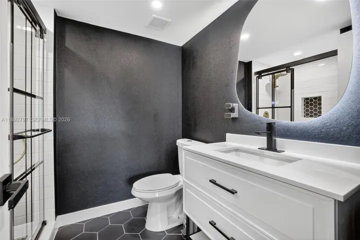 Super cool updated primary bathroom with glass shower enclosure, floating vanity, high hat lighting, backlit mirror