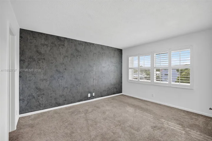 Primary Bedroom w/ Impact Windows, louvered shutters, wallpapered feature wall and newer carpet in amazing condition leading to ensuite bathroom and walk in closet