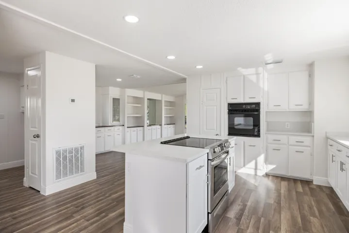 Kitchen with stainless steel electric stove, black oven, white cabinets, a center island