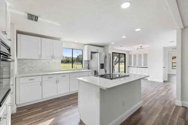 Kitchen with white cabinets, dark wood-type flooring, a center island, and tasteful backsplash