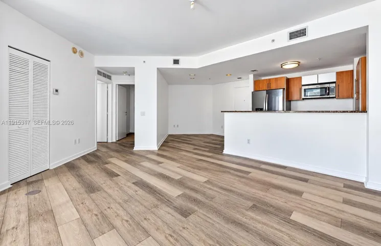 Wood-finish flooring throughout, kitchen with wood cabinetry, stainless steel appliances, and a built-in microwave, white louvered closet doors, and recessed lighting