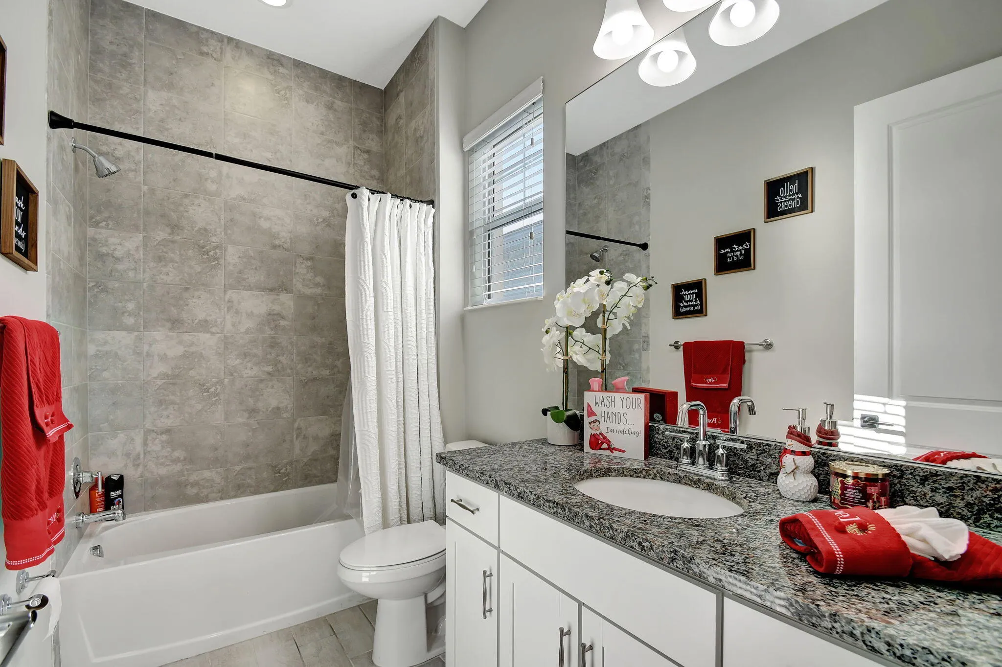 Bathroom featuring a tiled shower surround, integrated bathtub, white vanity with a dark speckled countertop, single basin sink, and a framed mirror