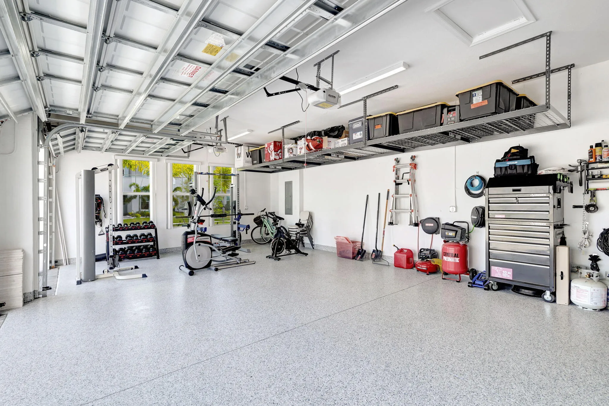 Garage with epoxy flooring, white walls, multiple windows, and overhead storage racks