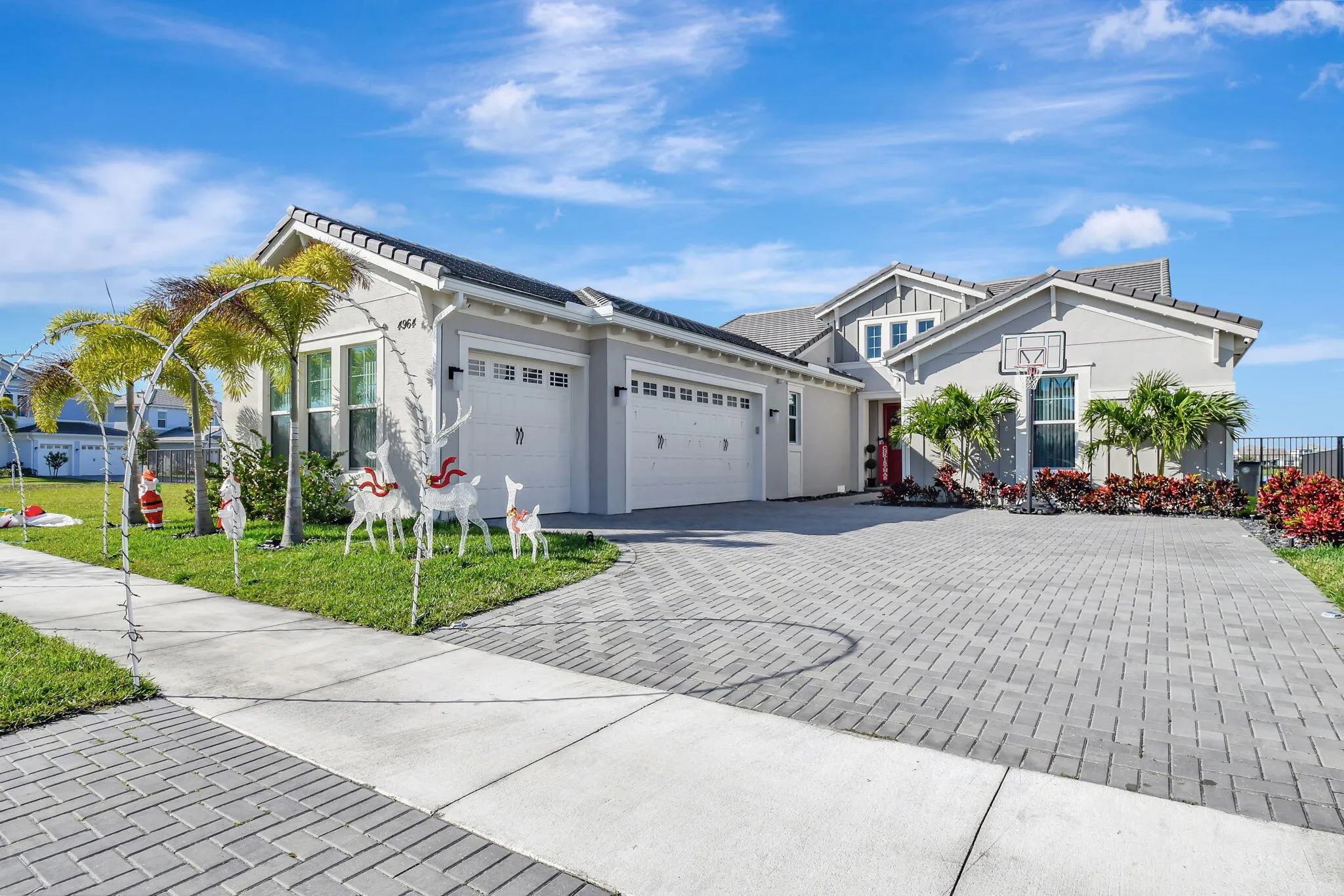 Light gray exterior with a dark shingle roof, paver driveway, and a two-car garage