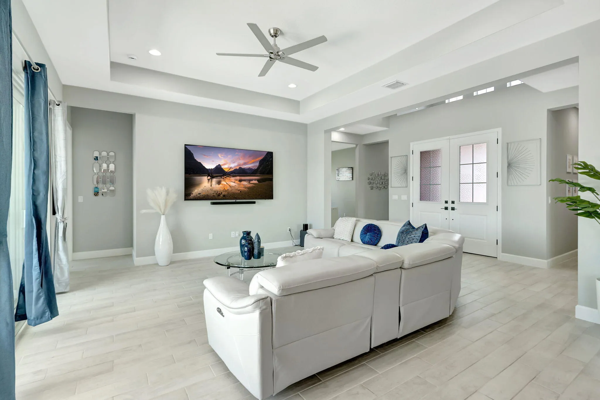 Tray ceiling with recessed lighting and a ceiling fan, light wood-finish flooring, and double doors with frosted glass panels