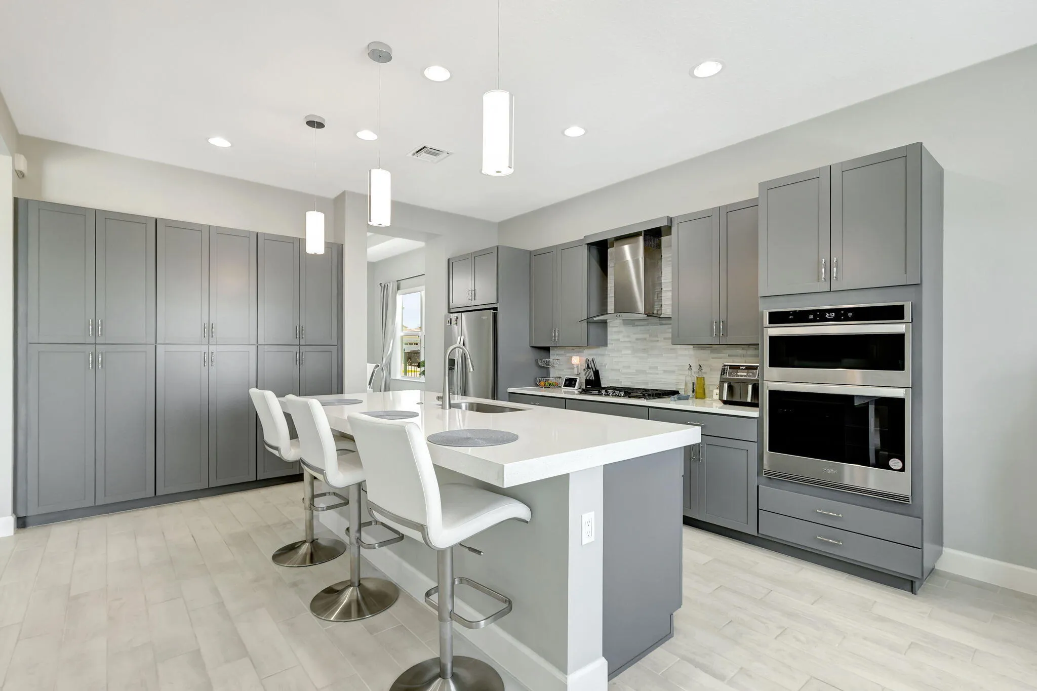 Kitchen featuring a large island with a composite countertop, wood-finish flooring, recessed lighting, and stainless steel appliances including a built-in oven and microwave