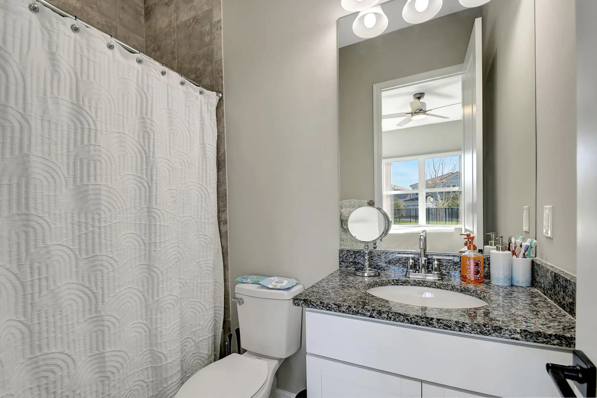 Bathroom with a stone-tile shower surround, white toilet, vanity with a granite countertop, undermount sink, and chrome faucet