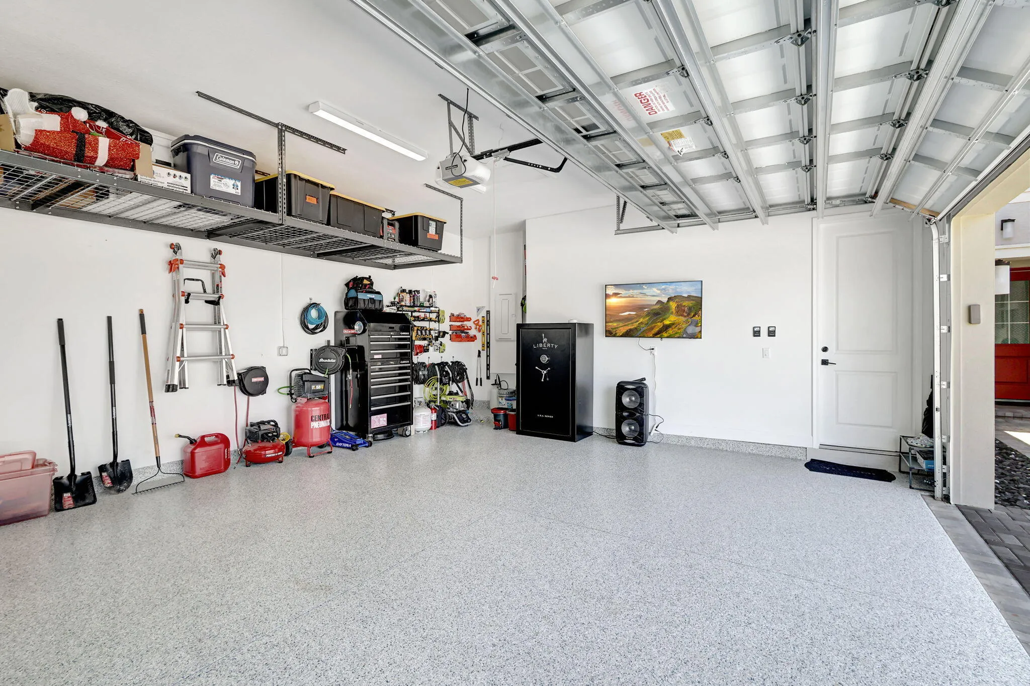 Epoxy-coated flooring, overhead storage racks, white paneled door, and exposed garage door mechanism
