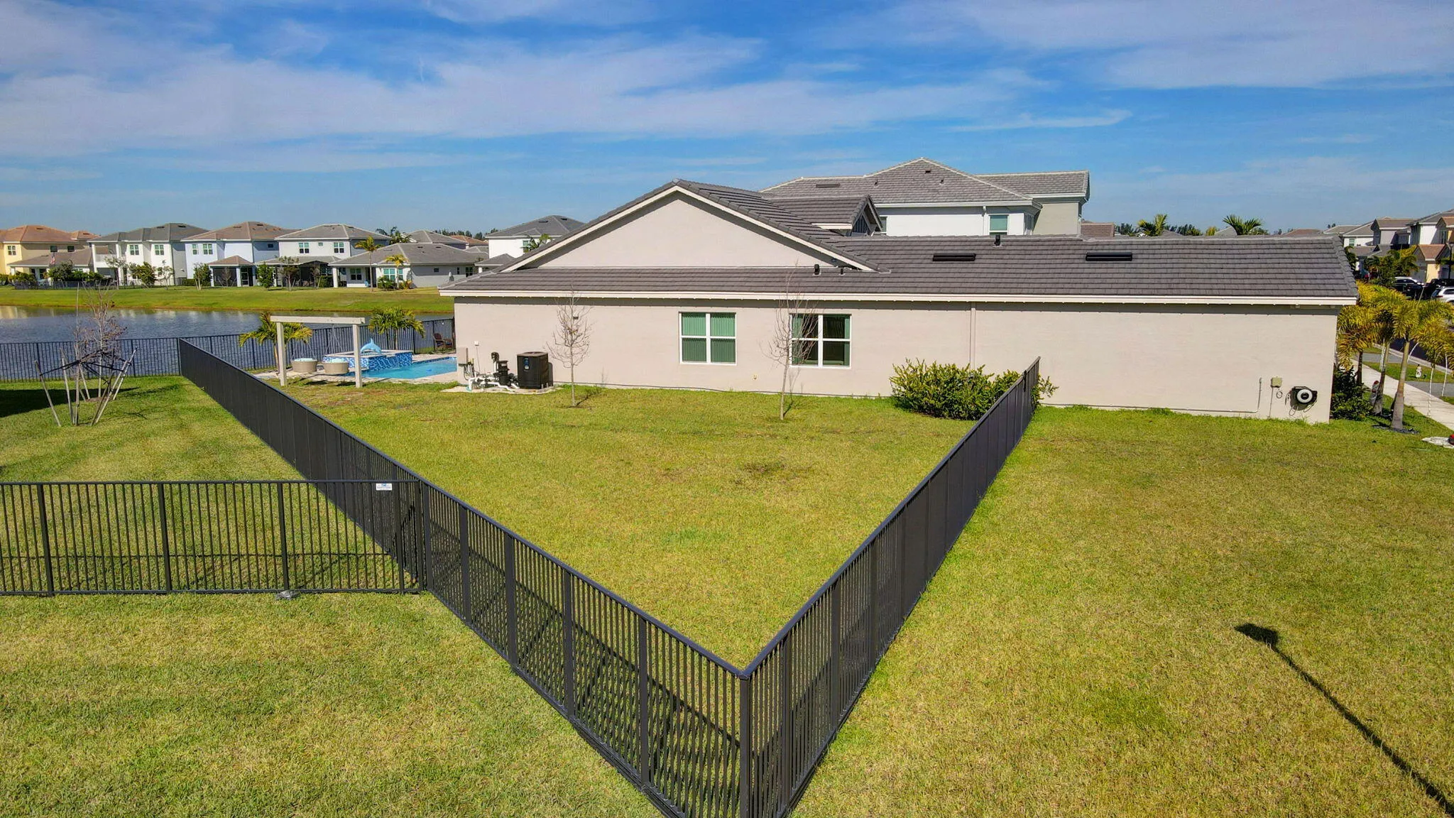 Expansive grass lawn with perimeter fencing, bordering a water feature, with an attached pergola and pool
