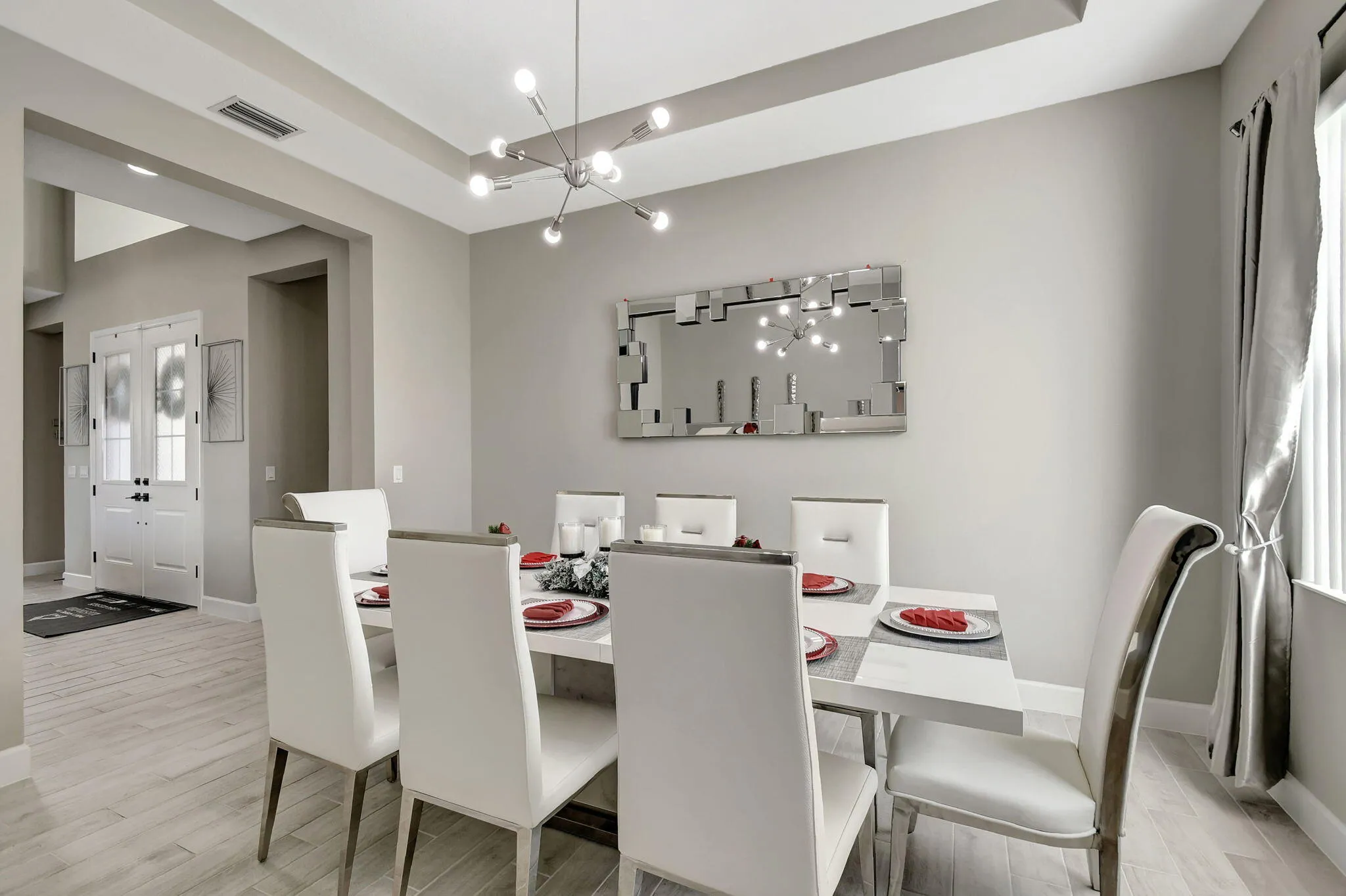 Tray ceiling with a modern chandelier, light-toned wood-finish flooring, and a mirrored wall accent