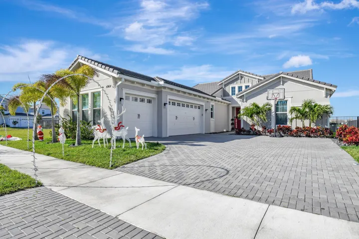 Light gray exterior with a dark shingle roof, paver driveway, and a two-car garage