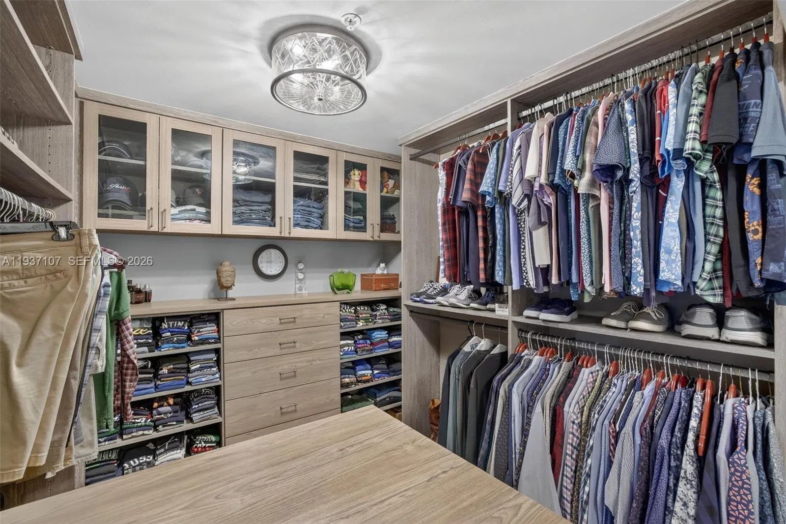 Custom walk in primary closet w/ tons of drawers on both sides of island and glass uppers