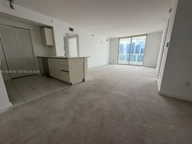 Open-concept interior featuring light-toned cabinetry, a peninsula countertop, ceramic tile flooring in the kitchen, wall-to-wall carpeting, and floor-to-ceiling glass sliding doors