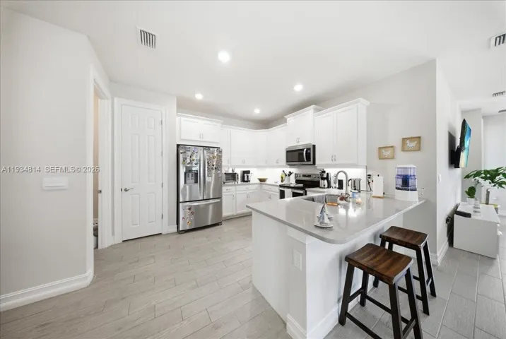 featuring appliances with stainless steel finishes, a kitchen bar, white cabinets