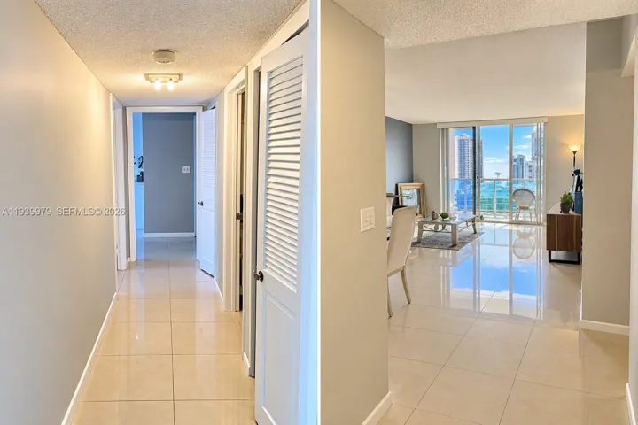 Interior hall featuring light-toned tile flooring, louvered closet doors, and access to an open-concept area with sliding glass doors leading to an exterior balcony
