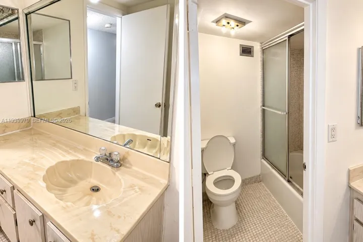 Bathroom featuring a vanity with a shell-shaped basin, oversized wall-mounted mirror, mosaic tile flooring, and a tub-shower combination enclosed by sliding glass doors