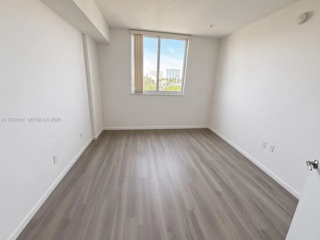 Neutral-toned interior room featuring wood-finish flooring, a large window, and vertical window blinds