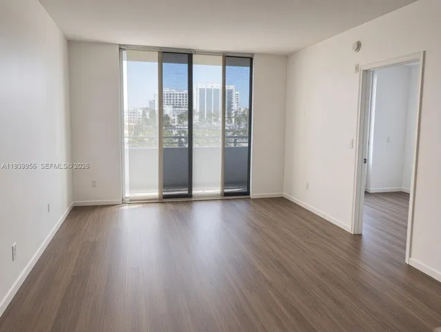 Wood-finish flooring, floor-to-ceiling sliding glass doors, and a private balcony featuring a metal railing