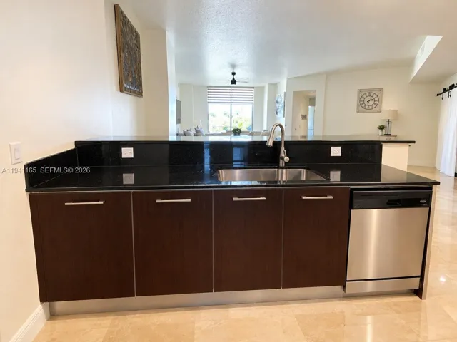 Kitchen peninsula featuring dark cabinetry, expansive stone countertops, stainless steel undermount sink with a gooseneck faucet, integrated stainless steel dishwasher, and stone flooring