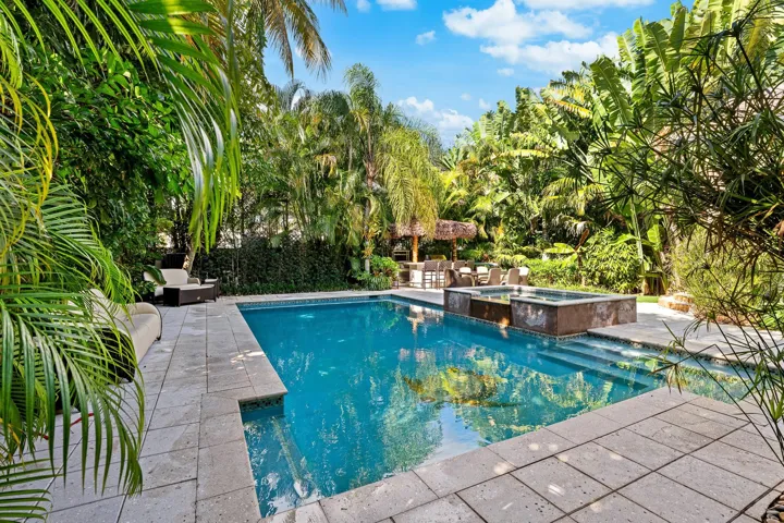 Resort-style pool and spa with tiki hut, BBQ, TV, and outdoor fridge.