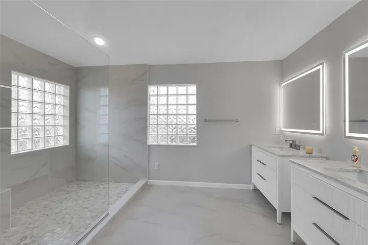 Brand new bathroom featuring a marble finish shower, linear drain, two vanities, recessed lighting, and light marble finish floors