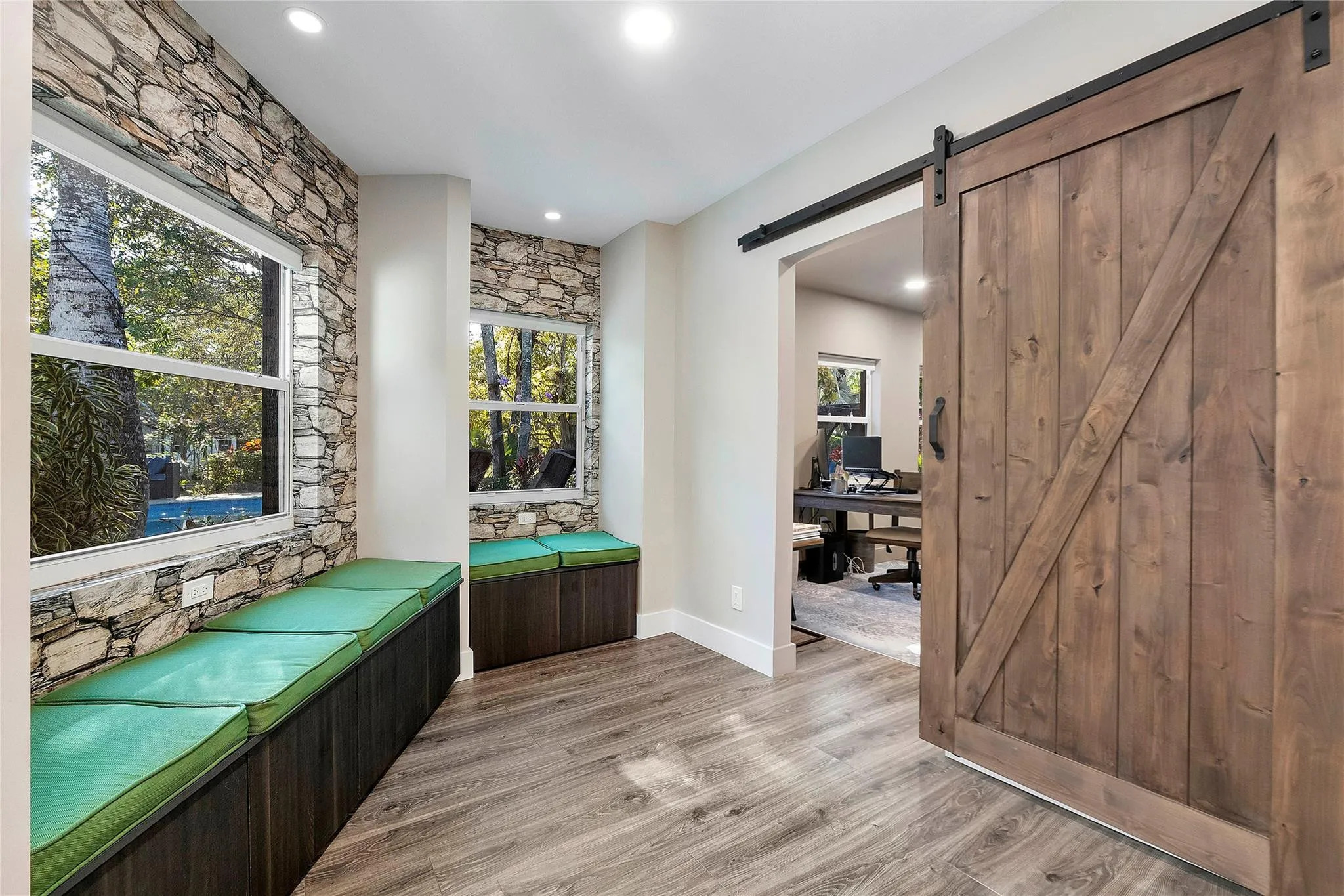 The quiet reading room with stone accent walls and a wide open barn door that leads into an office or den for complete privacy at the back of the house with the windows looking out onto the serene pool and garden.