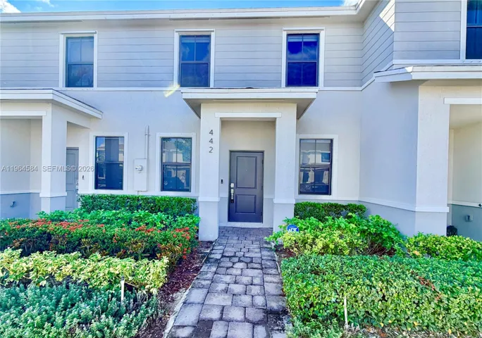 Two-story exterior featuring a neutral stucco and horizontal siding facade, covered entryway with stone-paver walkway, and manicured landscaping