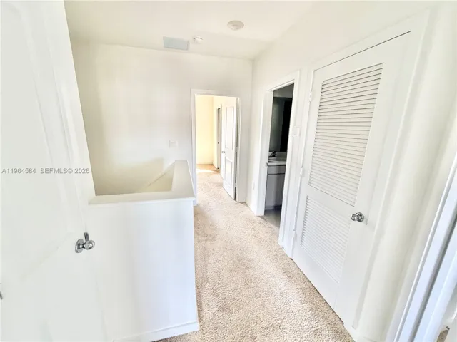 Hallway featuring wall-to-wall carpeting, paneled interior doors, and a louvered closet door