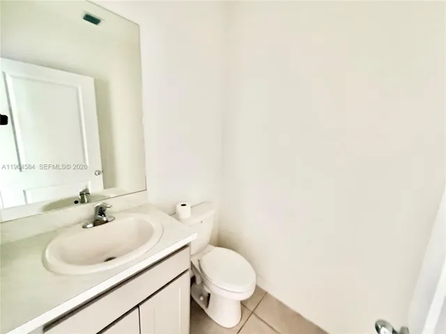 Vanity with an integrated sink, polished metal faucet, large frameless mirror, white cabinetry, and a white toilet